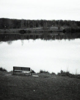 Photographie en noir et blanc d'un banc devant un lac